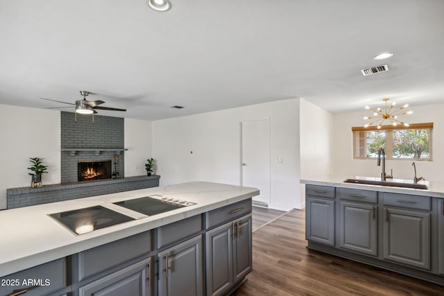 kitchen with a sink, light countertops, black electric cooktop, gray cabinets, and ceiling fan with notable chandelier