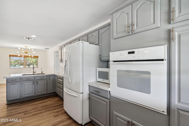 kitchen with visible vents, white appliances, gray cabinets, a sink, and a notable chandelier