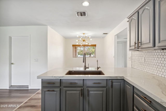 kitchen with a sink, gray cabinets, a peninsula, and visible vents