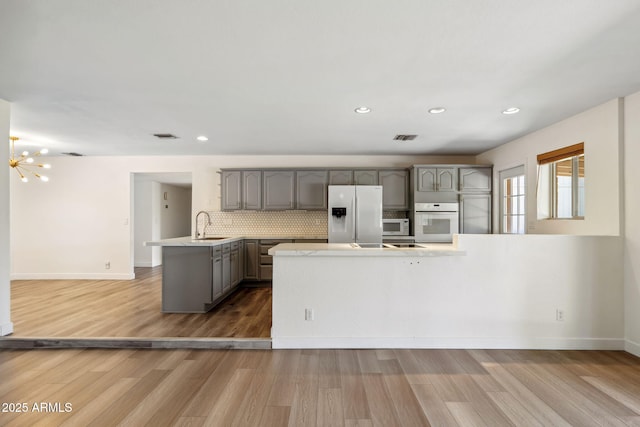kitchen featuring a sink, white appliances, light countertops, a peninsula, and gray cabinetry