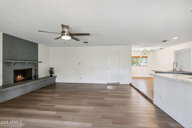 unfurnished living room with a brick fireplace, baseboards, light wood-type flooring, a sink, and ceiling fan with notable chandelier
