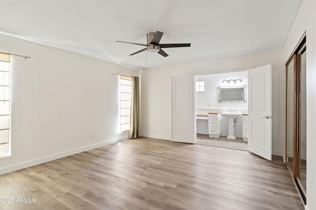 unfurnished bedroom with baseboards, multiple windows, light wood-type flooring, and connected bathroom