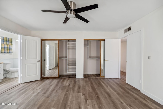 unfurnished bedroom featuring visible vents, two closets, baseboards, connected bathroom, and light wood-style flooring