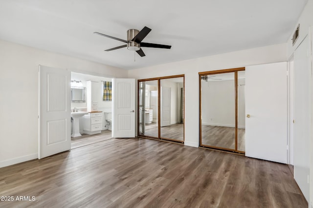 unfurnished bedroom with visible vents, two closets, wood finished floors, baseboards, and ensuite bath