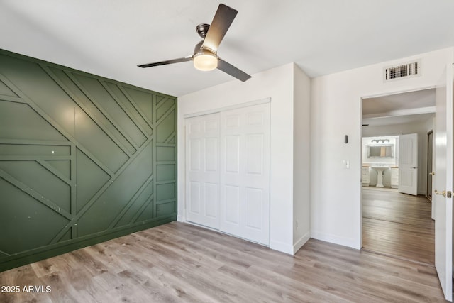 unfurnished bedroom with visible vents, a decorative wall, a closet, and light wood-type flooring