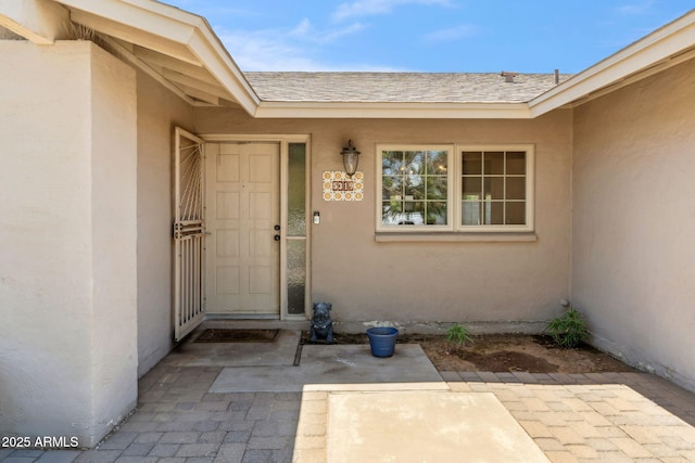 doorway to property with a patio, a shingled roof, and stucco siding