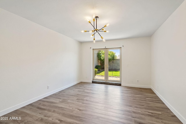 empty room featuring an inviting chandelier, baseboards, wood finished floors, and french doors