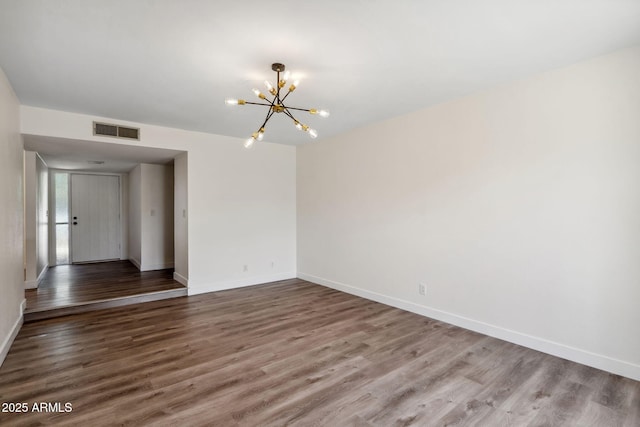 spare room with baseboards, visible vents, wood finished floors, and a chandelier