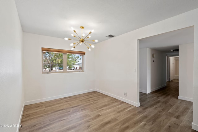 empty room with baseboards, visible vents, an inviting chandelier, and wood finished floors