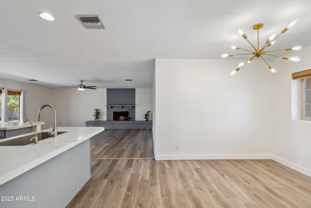 kitchen with visible vents, a fireplace, light wood-style floors, baseboards, and a sink
