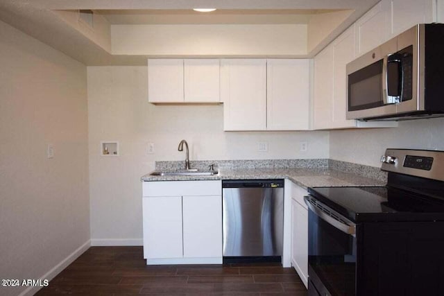 kitchen with sink, stainless steel appliances, white cabinets, light stone counters, and dark hardwood / wood-style flooring