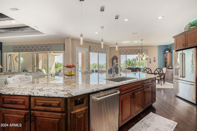 kitchen with a large island with sink, appliances with stainless steel finishes, sink, and decorative light fixtures