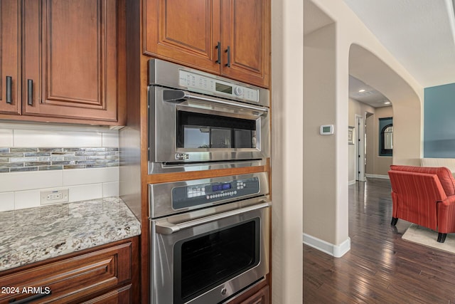 kitchen with light stone countertops, dark hardwood / wood-style floors, stainless steel double oven, and decorative backsplash