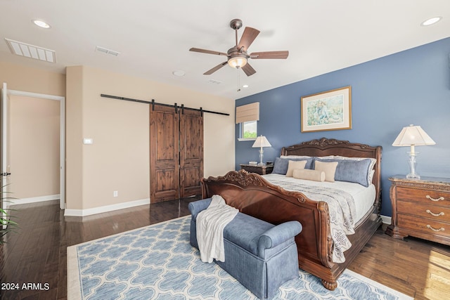 bedroom with ceiling fan, a barn door, and dark hardwood / wood-style flooring