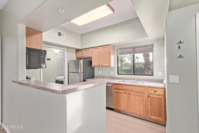 kitchen with stainless steel appliances, light countertops, visible vents, a sink, and a peninsula