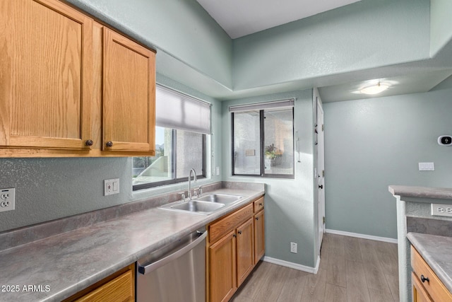 kitchen with light wood finished floors, light countertops, a sink, dishwasher, and baseboards