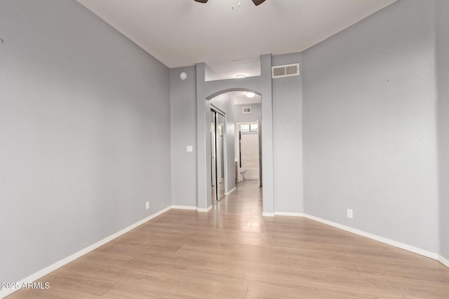 empty room featuring arched walkways, baseboards, visible vents, and light wood-style floors