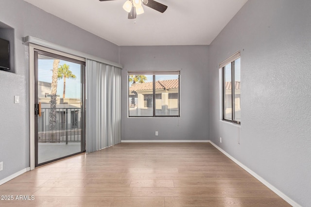 spare room featuring light wood-style floors, baseboards, a ceiling fan, and a textured wall