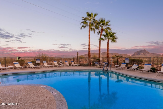 pool at dusk with a patio area, a community pool, fence, and a mountain view