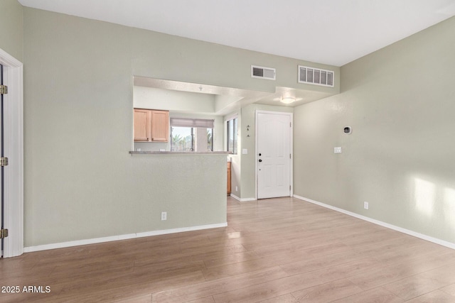 spare room featuring light wood-type flooring, visible vents, and baseboards