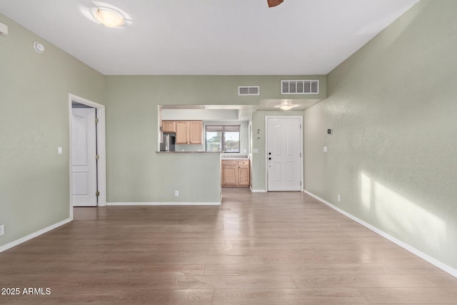 unfurnished living room featuring visible vents, light wood-style flooring, and baseboards