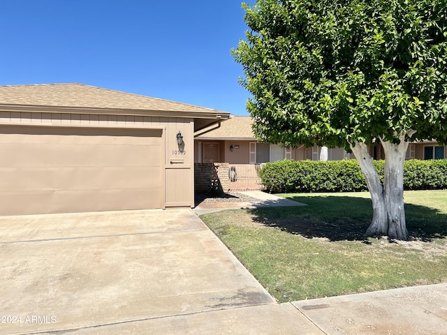 view of front of house with concrete driveway, a garage, roof with shingles, and a front lawn