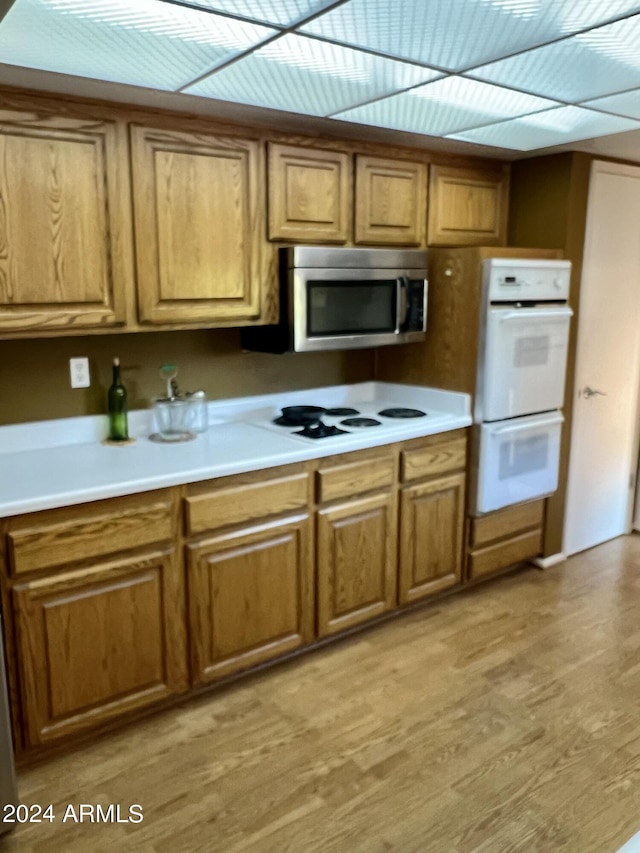 kitchen featuring white appliances, light wood-type flooring, brown cabinetry, and light countertops