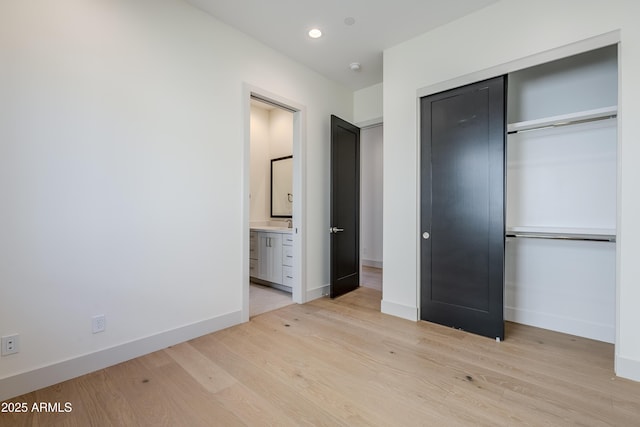 unfurnished bedroom featuring light hardwood / wood-style flooring, ensuite bath, and a closet