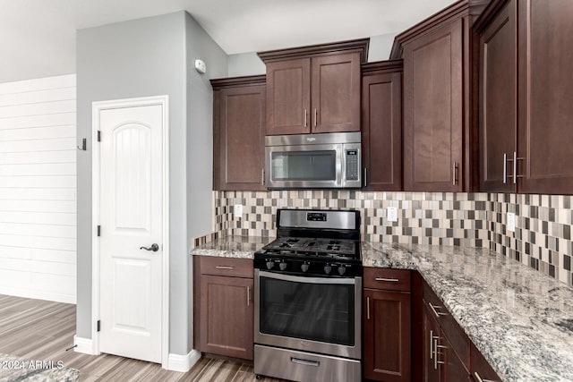 kitchen featuring light stone countertops, stainless steel appliances, backsplash, light hardwood / wood-style floors, and dark brown cabinets