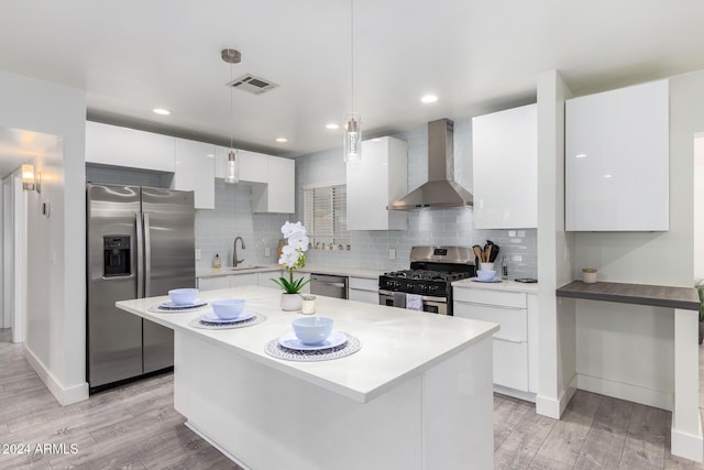 kitchen featuring wall chimney exhaust hood, hanging light fixtures, stainless steel appliances, light hardwood / wood-style flooring, and white cabinets