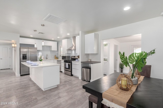 kitchen featuring pendant lighting, wall chimney exhaust hood, a kitchen island, white cabinetry, and stainless steel appliances