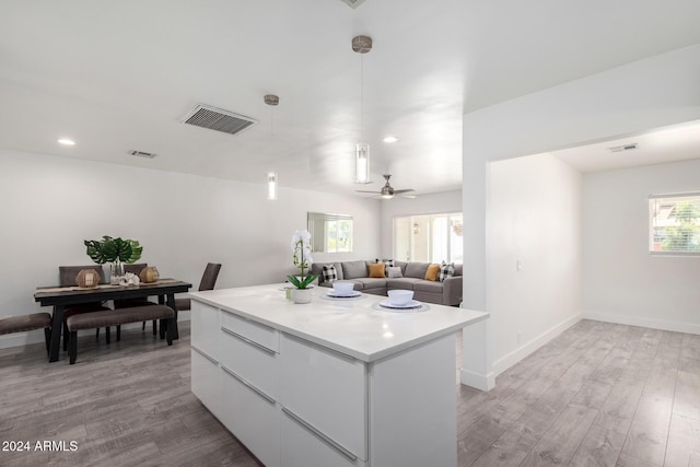 kitchen with light hardwood / wood-style floors, ceiling fan, a kitchen island, and white cabinetry