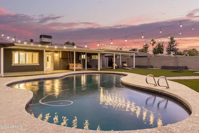 pool at dusk featuring a lawn, cooling unit, and a patio area