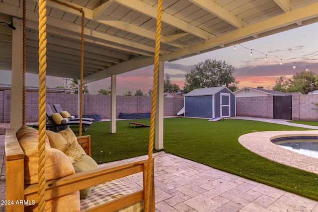 patio terrace at dusk with a fenced in pool, outdoor lounge area, a lawn, and a storage unit