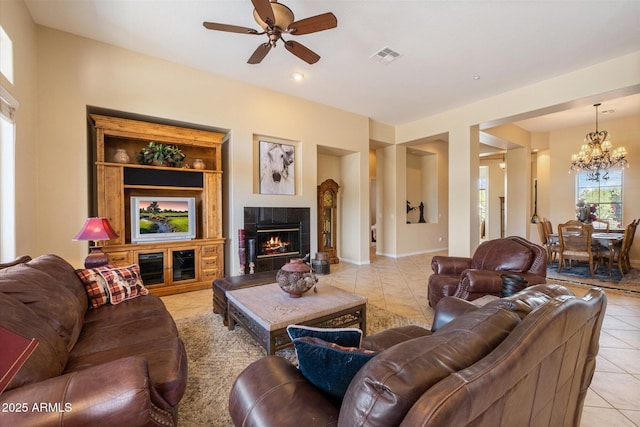 living room with a tile fireplace, baseboards, light tile patterned floors, ceiling fan with notable chandelier, and visible vents