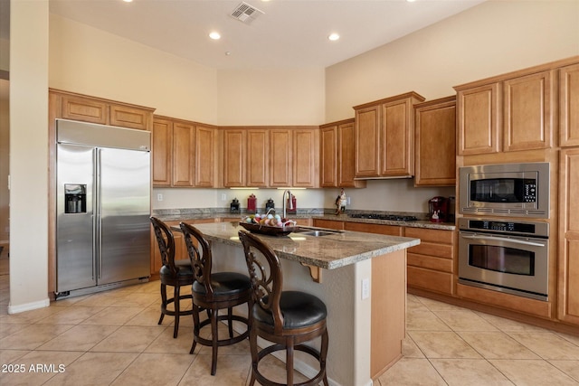 kitchen featuring light tile patterned floors, a center island with sink, a sink, built in appliances, and visible vents