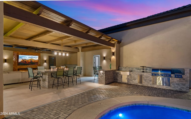 pool at dusk with outdoor wet bar, a patio, and area for grilling