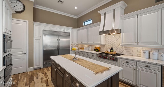 kitchen with stainless steel appliances, white cabinets, ornamental molding, decorative backsplash, and wall chimney exhaust hood