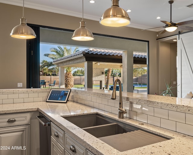 kitchen with light stone countertops, a barn door, ornamental molding, and a ceiling fan