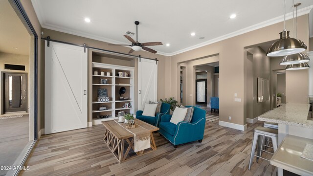 living room featuring a barn door, light hardwood / wood-style flooring, ceiling fan, and crown molding