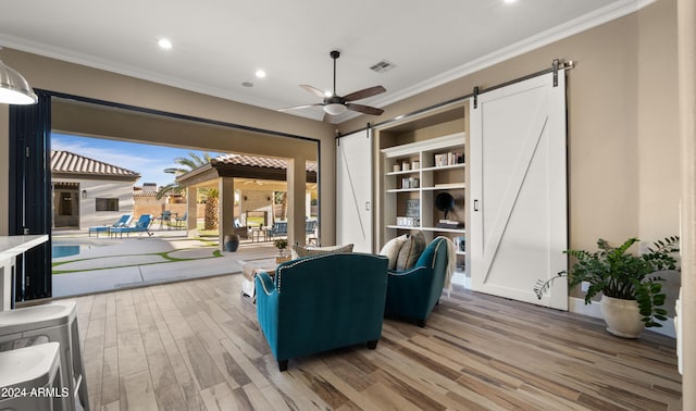 living room featuring ceiling fan, a barn door, wood-type flooring, and ornamental molding