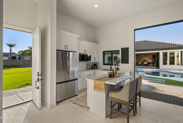 kitchen featuring a high ceiling, white cabinets, light countertops, appliances with stainless steel finishes, and a center island