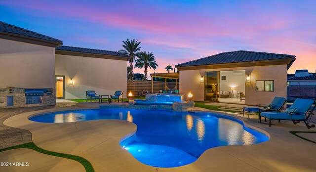 pool at dusk featuring a pool with connected hot tub, fence, a patio, and area for grilling