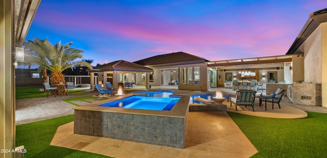 patio terrace at dusk with outdoor dry bar, an in ground hot tub, fence, and a fenced in pool