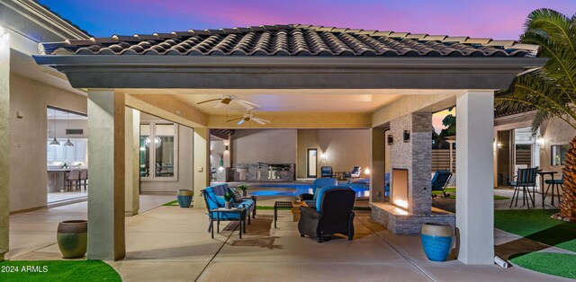 patio terrace at dusk with exterior kitchen, a swimming pool, and a ceiling fan