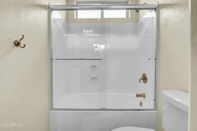 full bathroom featuring enclosed tub / shower combo, a textured wall, and toilet