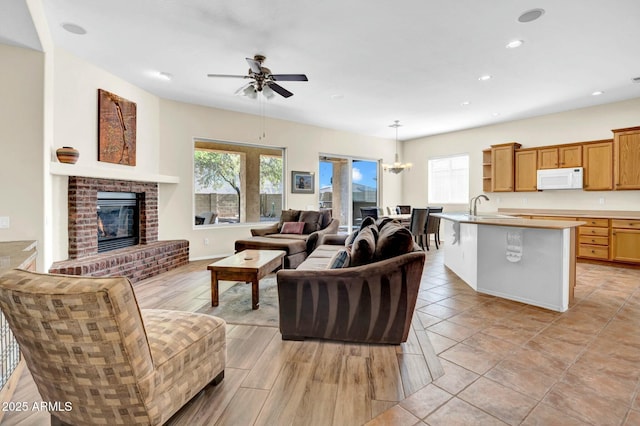 living room with light wood finished floors, a fireplace, ceiling fan with notable chandelier, and recessed lighting