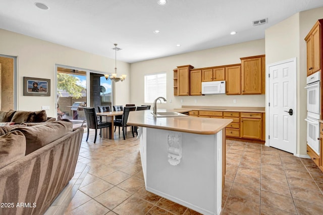 kitchen featuring white appliances, visible vents, light countertops, pendant lighting, and a sink