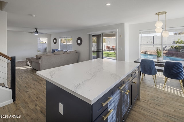 kitchen featuring dark wood-type flooring, light stone counters, decorative light fixtures, a center island, and ceiling fan