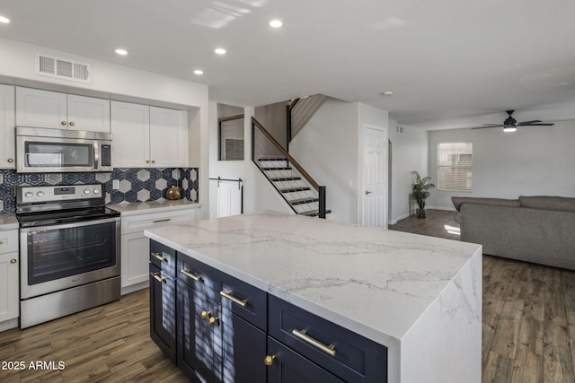 kitchen with white cabinetry, stainless steel appliances, a center island, and light stone countertops